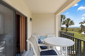 A balcony with a white table and chairs, a view of the beach, and a palm tree. - Cozy Two Level Condo Overlooking the Ocean and Beachside Pool! (St. Augustine)