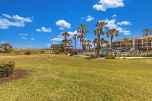A golf course with a clubhouse, palm trees, and a hotel in the background.
