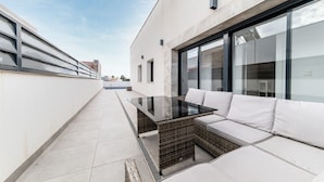 A modern outdoor patio with a glass-top table and white cushioned seating. - Villa Armonia - Heated Pool - Countryside Charm - by OYOOSTAYS (Daya Nueva)