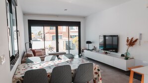 A modern living room with a dining area, large windows, a flat-screen TV, and a white console. - Villa Armonia - Heated Pool - Countryside Charm - by OYOOSTAYS (Daya Nueva)