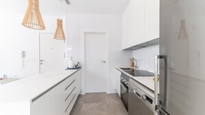 A modern kitchen with white cabinetry, stainless steel appliances, and two wooden pendant lights. - Villa Armonia - Heated Pool - Countryside Charm - by OYOOSTAYS (Daya Nueva)
