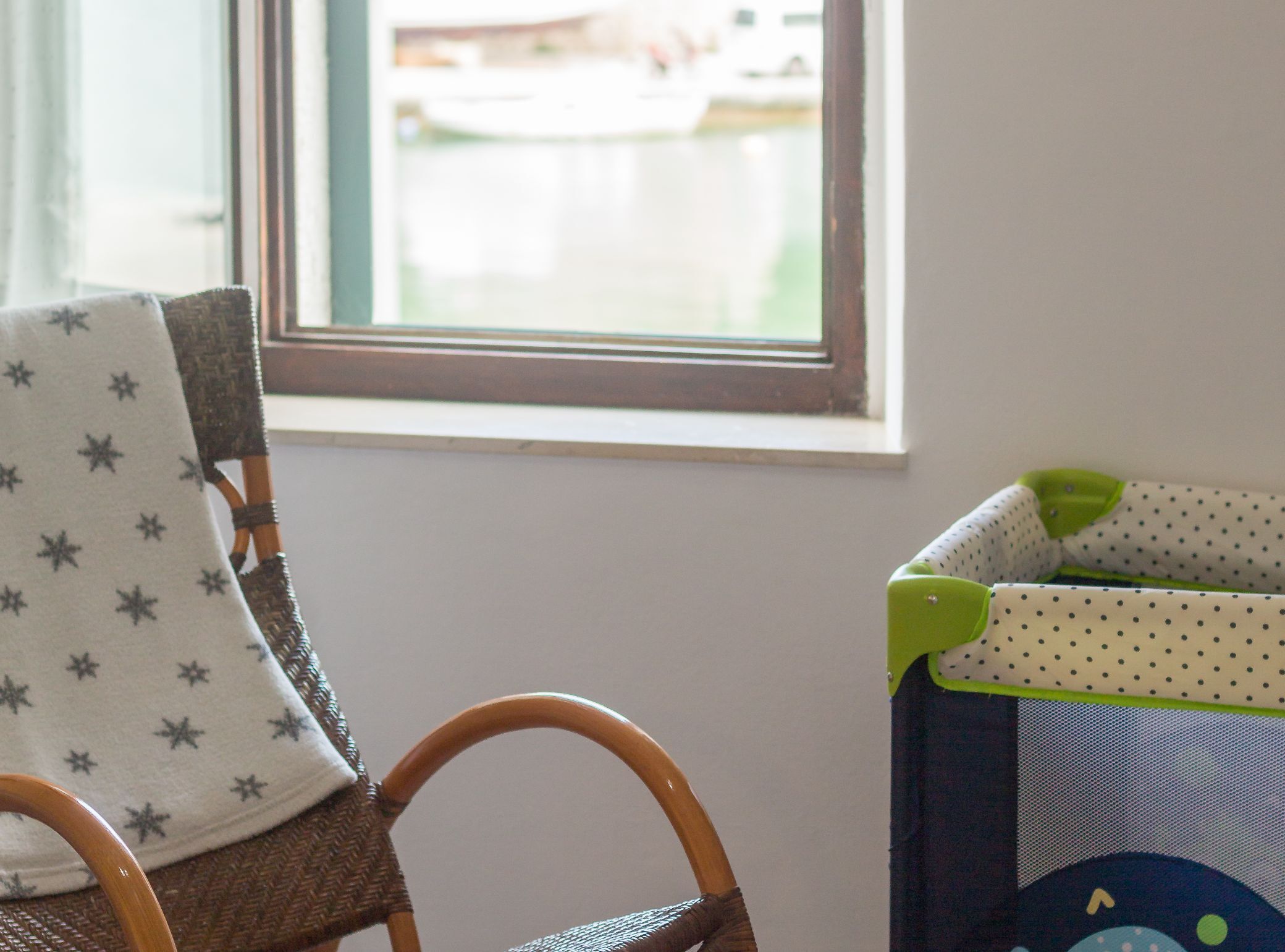 Una silla de mimbre con un cojín estampado con estrellas y un corralito infantil con diseño de lunares.