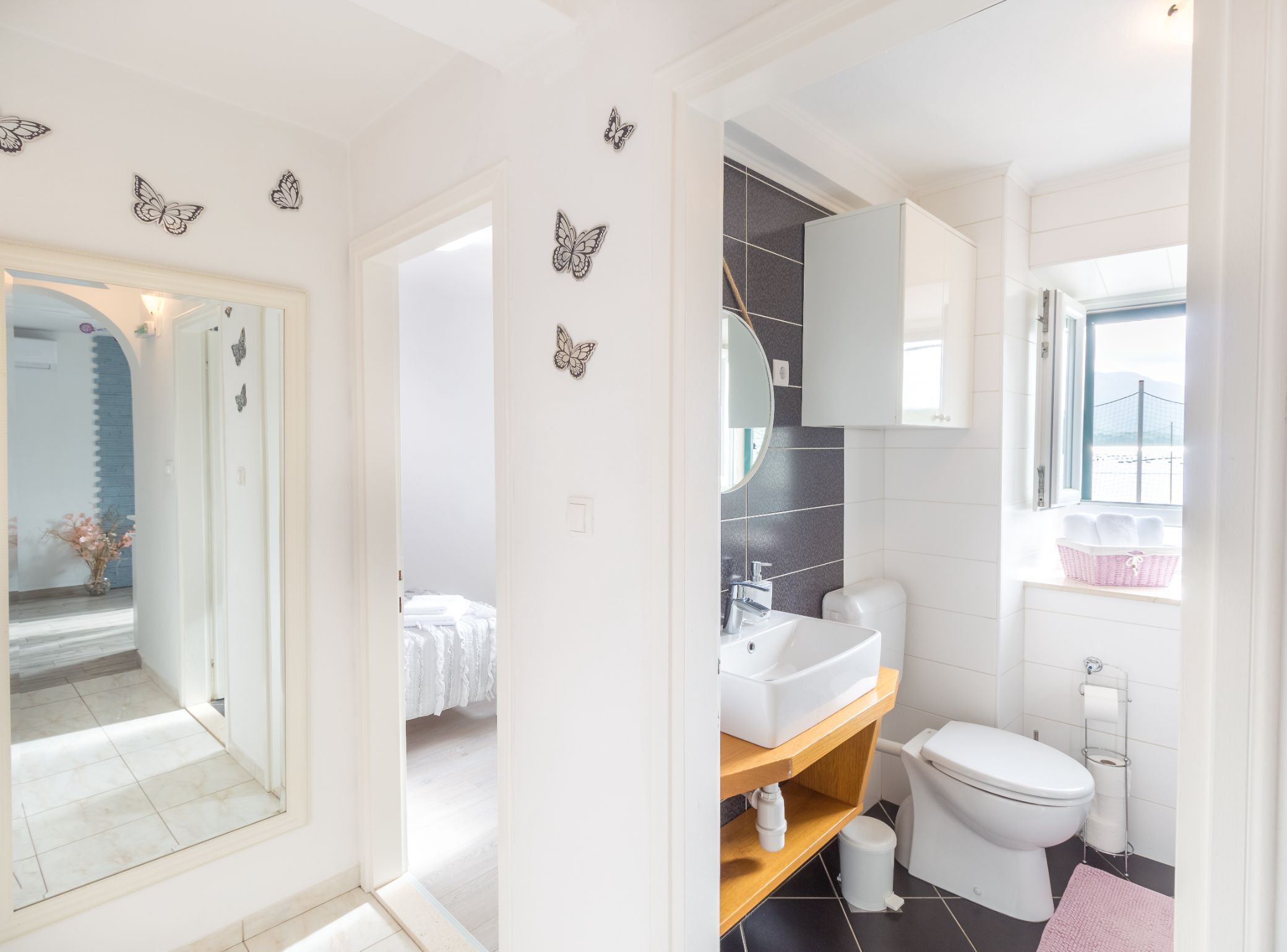 Une salle de bain moderne avec un lavabo, des toilettes et un meuble-lavabo blancs. Les murs sont décorés de motifs de papillons et il y a une fenêtre avec vue.