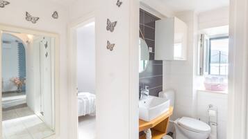 Une salle de bain moderne avec un lavabo, des toilettes et un meuble-lavabo blancs. Les murs sont décorés de motifs de papillons et il y a une fenêtre avec vue.