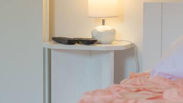 A bed with a pink blanket, a bedside table with a lamp, and two remote controls.