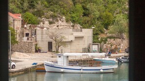 A boat docked at a marina with a stone building and rocky hillside in the background. - Holiday Home Riva (Ston)