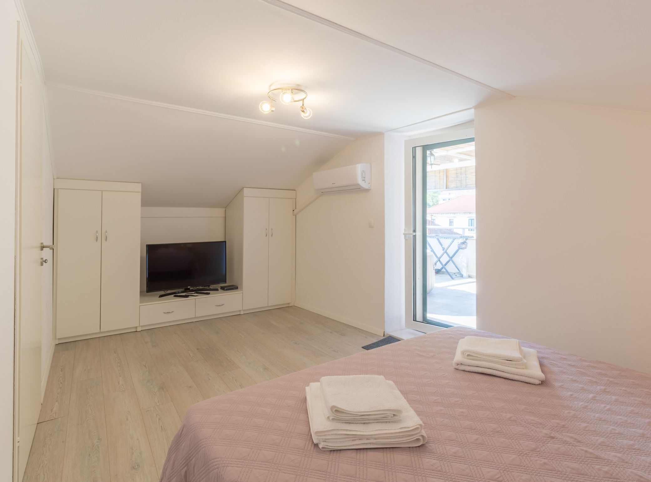 A bedroom with a TV, wardrobe, and a balcony view.