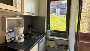 A compact kitchen with a built-in microwave, coffee maker, and toaster. A window offers a view of a green landscape and buildings. - 50m from ski lifts, 2nd floor, view ski slopes, balcony, tv, 28m², La Plagne (La Plagne)