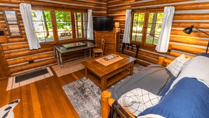 Habitación tipo cabaña de madera con una cama de madera, un televisor, un escritorio y una silla, y ventanas amplias.