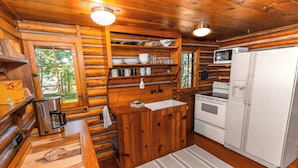Cocina de cabaña de madera con cafetera, microondas, refrigerador y estantes de madera.