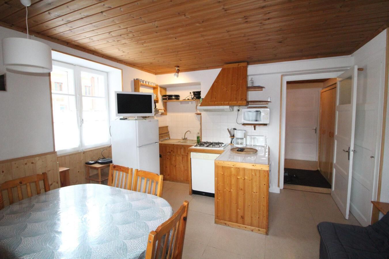 A compact kitchen with wooden cabinets, a refrigerator, a microwave, and a dining area with a table and chairs.
