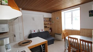 A cozy room with a wooden ceiling, a sofa, a dining table with chairs, a kitchen area with a stove and microwave, and a window providing natural light. - Ground floor, tv, ski locker, 55m², Val Cenis (Lanslebourg-Mont-Cenis)