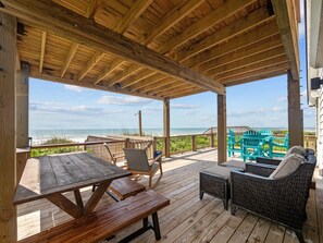 Een houten terras met een picknicktafel en rieten meubilair met uitzicht op een strand.