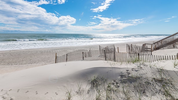 Een strand met een houten hek en een trap die naar het zand leidt.