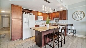 Eine moderne Küche mit Holzschränken, einem weißen Kühlschrank, einer zentralen Kochinsel mit Barhocker und einer Wanddekoration.