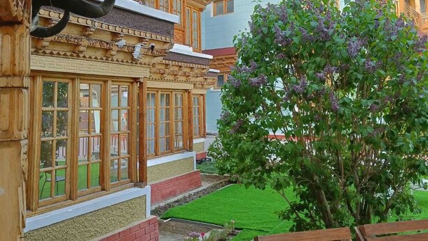 Un edificio tradicional con elaboradas esculturas de madera y un jardín cuidado con un árbol y bancos.