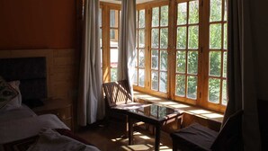 Una habitación con cama, una silla, una mesa y ventanas amplias con cortinas.