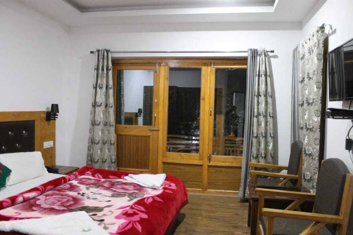 Un dormitorio con cama, una puerta de madera que da a un balcón y una silla.