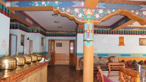Un interior tradicional con un mostrador de recepción de madera, un pilar central con diseños intrincados y una zona de estar con cojines.