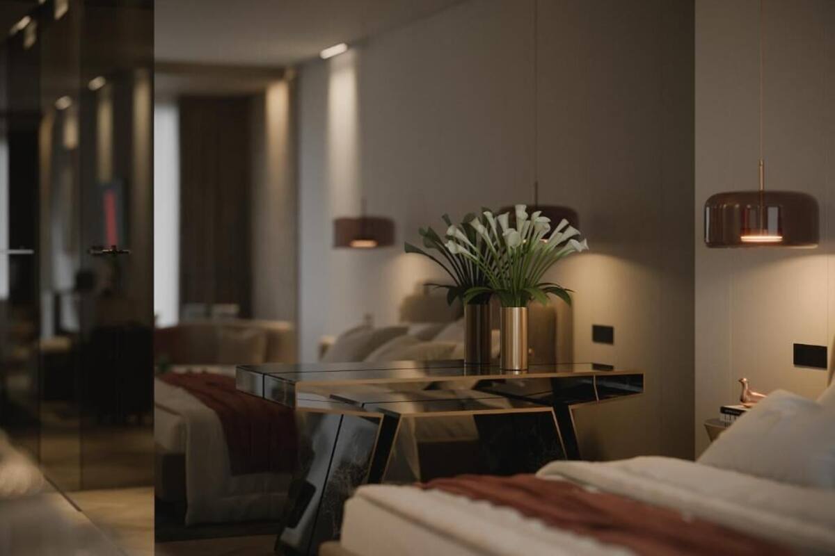 Ein modernes Hotelzimmer mit Glastisch, einem Bett mit weißer und brauner Decke, einer Vase mit weißen Blumen und einer Pendelleuchte.