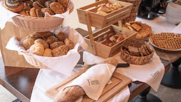 Variedad de panes y pasteles exhibidos sobre una mesa de madera, con cestas y cajas de madera que contienen productos horneados.