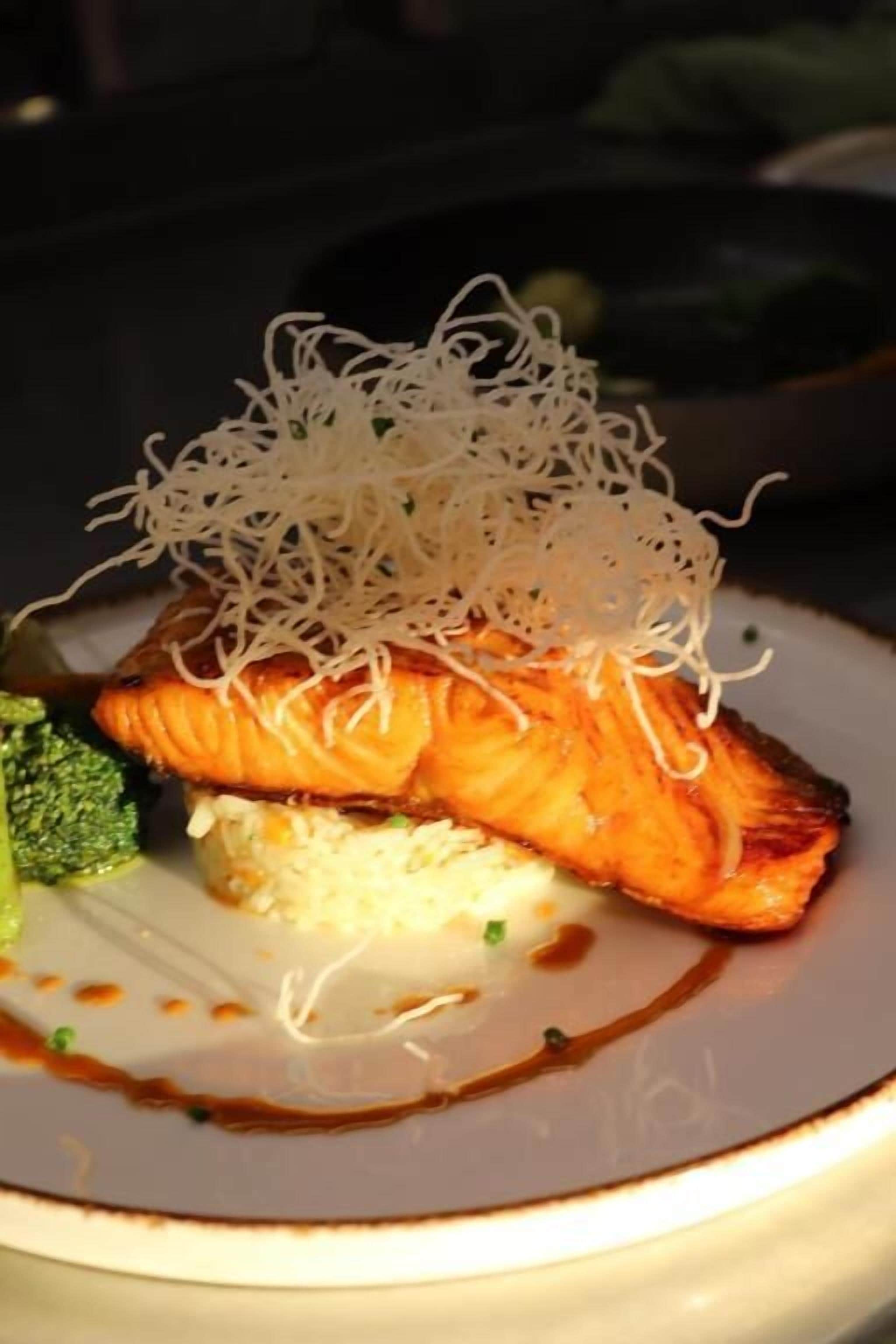 A plate with grilled salmon, a side of rice, and a garnish of thin noodles.