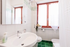 A bathroom with a white sink, a toilet, and a window with a red frame.