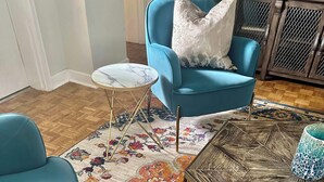 A living room with a blue armchair, a small round table, and a colorful floral rug. - FIFA 2026 Walk to Stadium | 2BR Unit 10G ATL (Atlanta)
