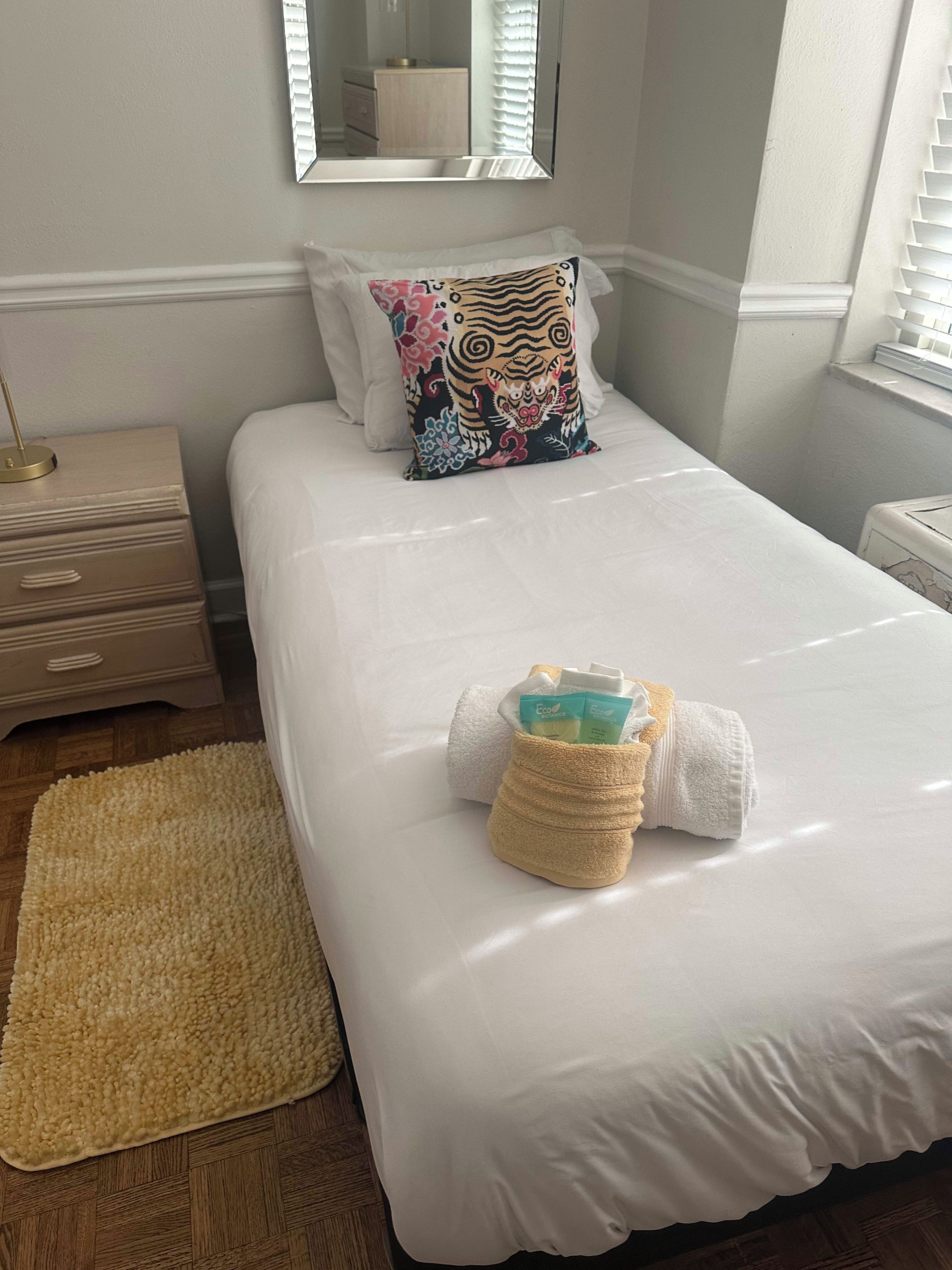 A neatly made bed with a white duvet, a decorative pillow, and a small towel with toiletries.