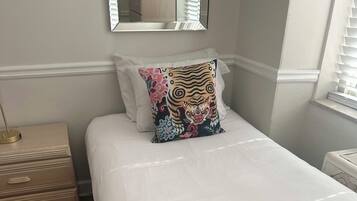 A neatly made bed with a white duvet, a decorative pillow, and a small towel with toiletries.