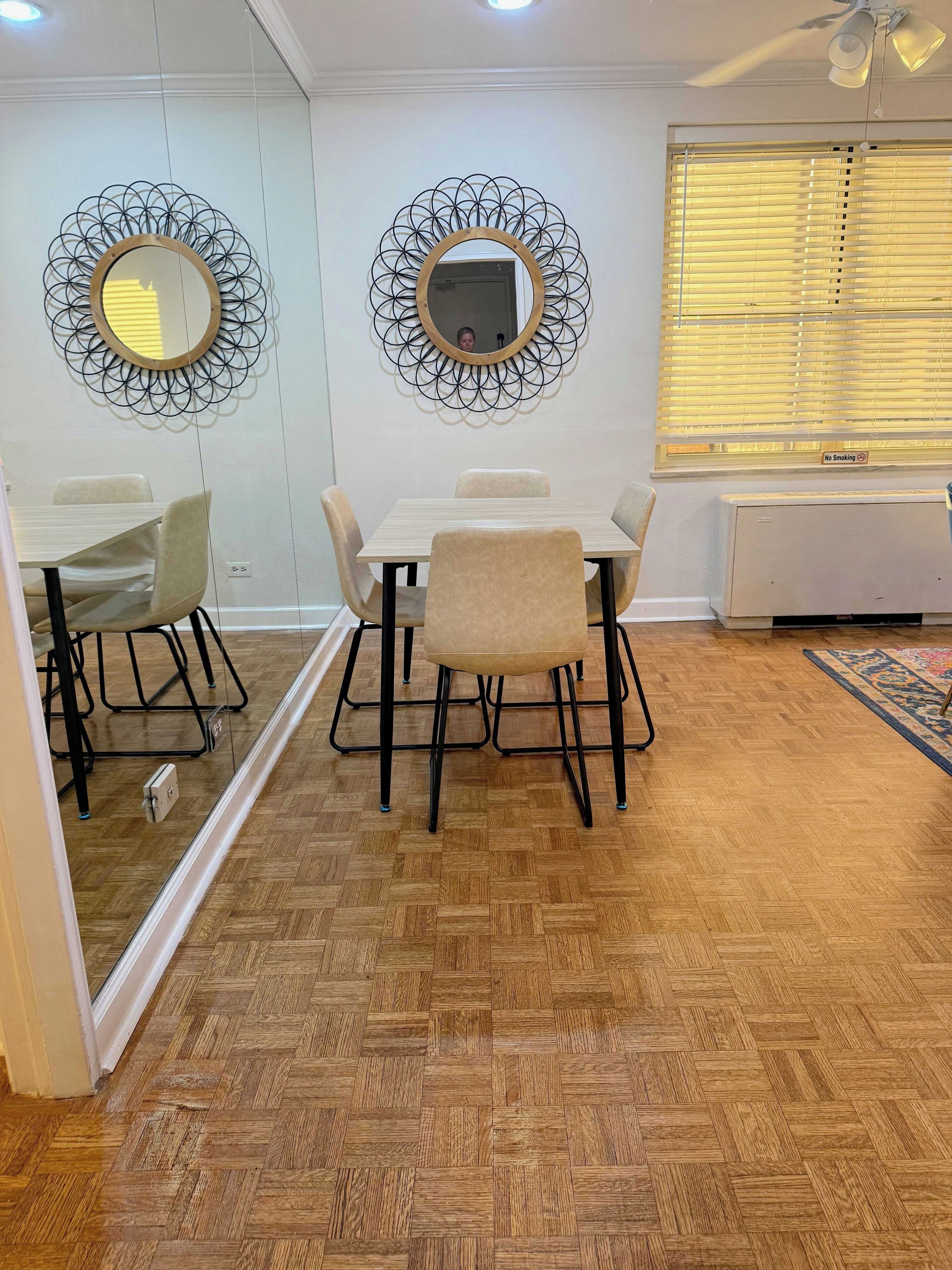 A dining area with a wooden herringbone floor, a white table with four chairs, and decorative wall mirrors.
