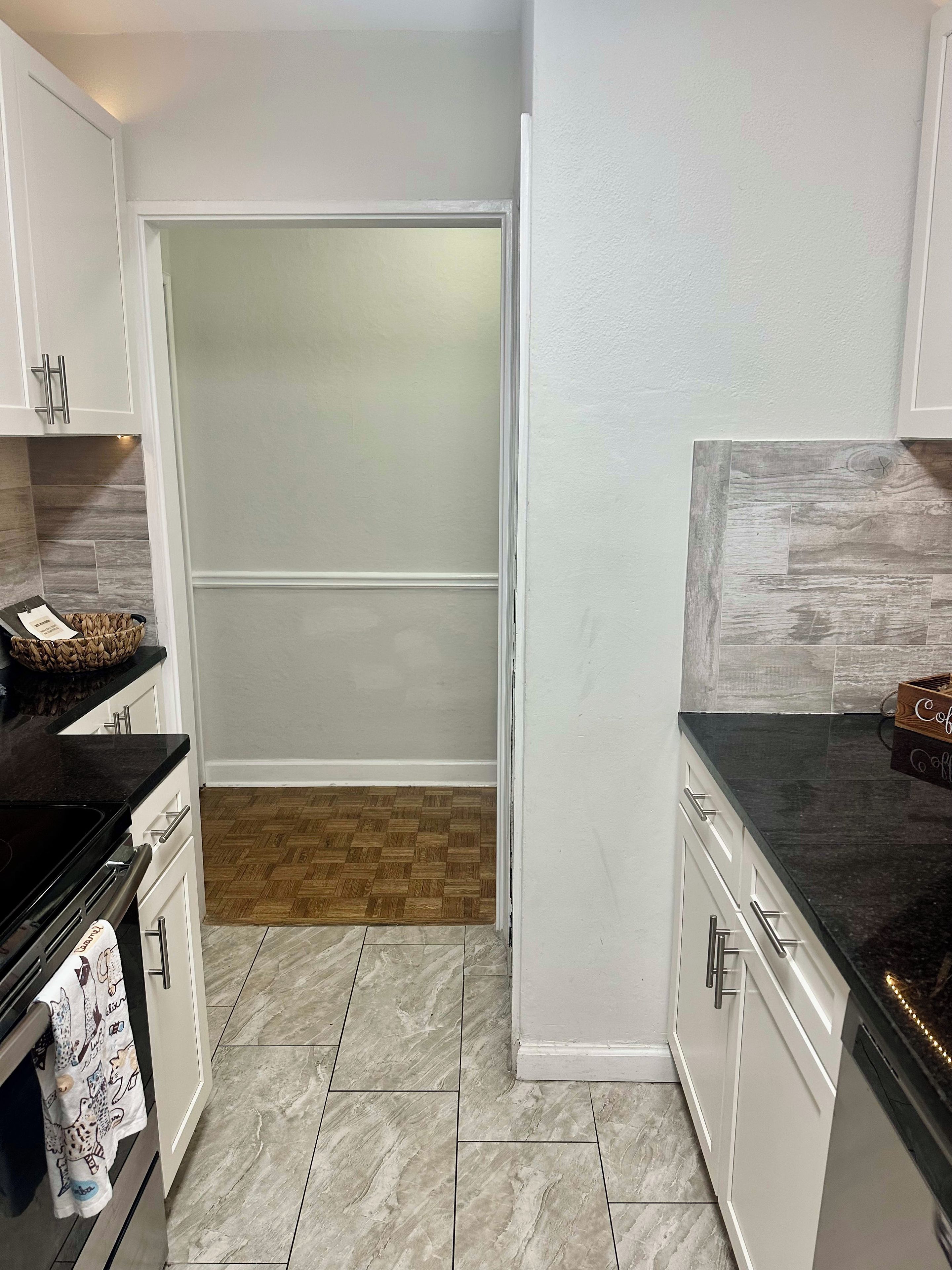 A kitchen with white cabinets, a black countertop, and a wooden floor.