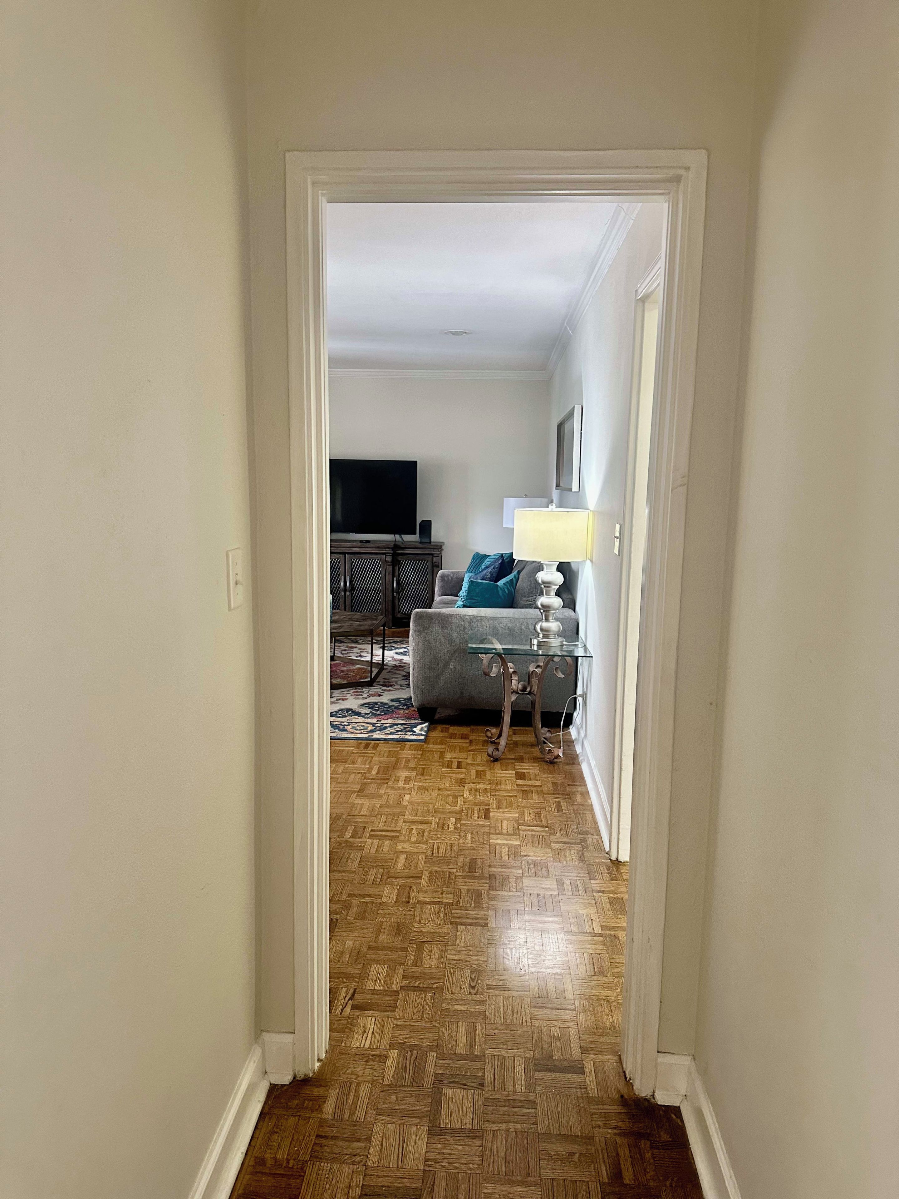 A hallway leading to a living room with a television, sofa, and lamp.