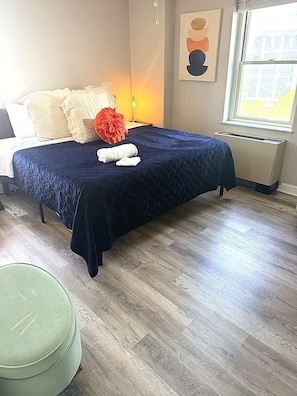 A neatly made bed with a dark blue bedspread, a green ottoman, and a large decorative flower. - FIFA 2026 Walk to Stadium | 1BR Unit 8B ATL (Atlanta)