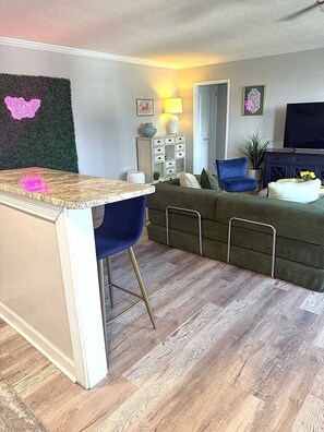 A living room with a sofa, a blue chair, a small table, and a TV.