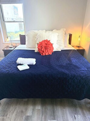 A hotel room with a large bed, a window with a view, a bedside table with a lamp, and a nightstand with a lamp.