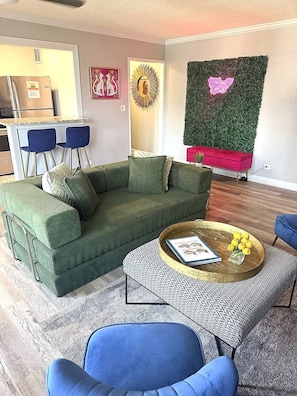 Una sala de estar con un sofá verde, una mesa de centro y sillas azules.