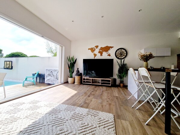A modern living room with a flat-screen TV, world map wall art, and a pool outside. - Private 3-Bedroom Vacation Home in Agde (Agde)