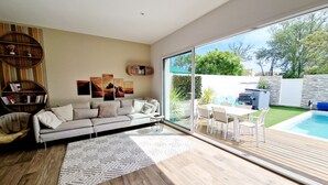 A modern living room with a sofa, a coffee table, and a rug. There is a glass door leading to a patio with a pool and outdoor furniture. - 3 bedroom private vacation home in agde (Agde)