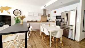A modern kitchen with white cabinetry, stainless steel appliances, and a dining area with white chairs and a black table. - 3 bedroom private vacation home in agde (Agde)