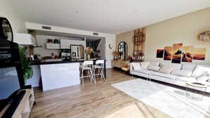 A modern kitchen with white cabinetry, a central island, and a dining area with white chairs. - 3 bedroom private vacation home in agde (Agde)