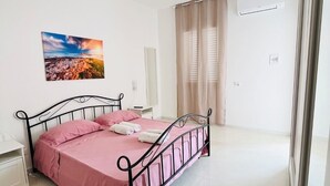 Une chambre à coucher avec un lit, une table de chevet, un miroir et une fenêtre avec des rideaux.