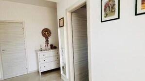 Un couloir avec une armoire blanche, une petite table ornée d’objets décoratifs et des tableaux encadrés accrochés au mur.