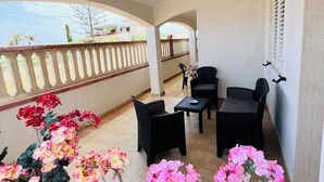 Un balcon agrémenté de meubles en osier noir, d’une petite table et de plantes en pot.