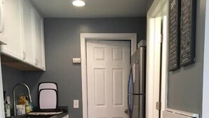 A compact kitchen with white cabinets, a black rug, a stainless steel refrigerator, and a trash can. - Pet-Friendly House Steps from Midtown Excitement (Omaha)