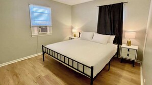 A bedroom with a bed, two bedside tables with lamps, a ceiling fan, a window with blinds, and a dark curtain. - Steps From UNMC, Dining, Explore Midtown (Omaha)