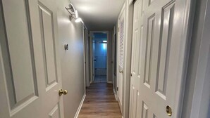 A narrow hallway with white doors, a wooden floor, and a ceiling light fixture. - Steps From UNMC, Dining, Explore Midtown (Omaha)