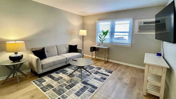 A living room with a sofa, a coffee table, a lamp, a small side table, a plant, and a TV mounted on the wall. - Steps From UNMC, Dining, Explore Midtown (Omaha)