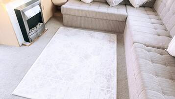 A living room with a beige sofa, a white rug, and a small side table with a lamp.