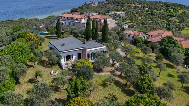 A coastal property with multiple buildings, including a large villa with a red-tiled roof, surrounded by olive trees and a view of the sea. - MGH Luxury - Villa Sirmione (Sirmione)